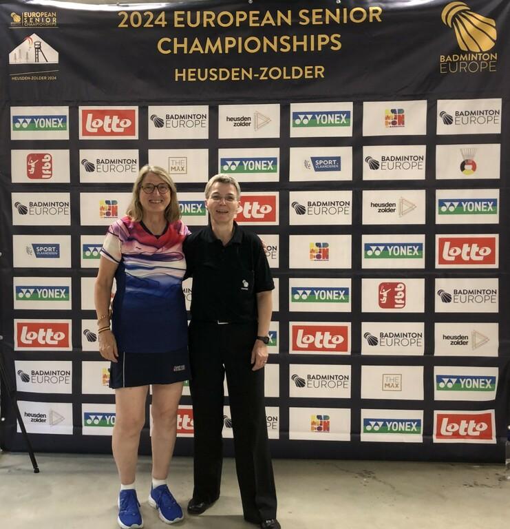 Conny und Jutta bei der EM der Altersklassen in Belgien Zwei Frauen stehen vor einem Banner der 2024 European Senior Championships in Heusden-Zolder.