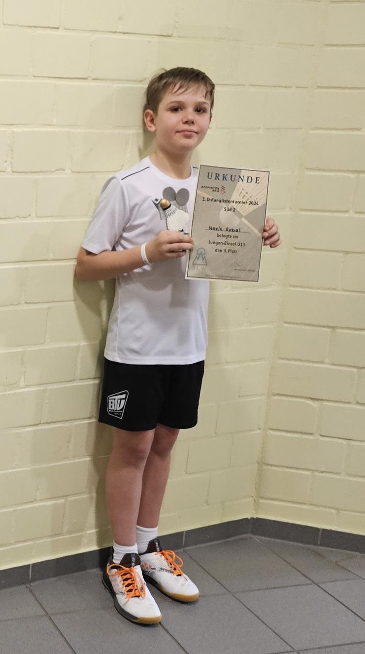 Henk Gebel auf Platz 3 im JE U13 Junge in Sportkleidung hält eine Urkunde und einen Pokal in der Hand, steht vor einer hellen Wand.